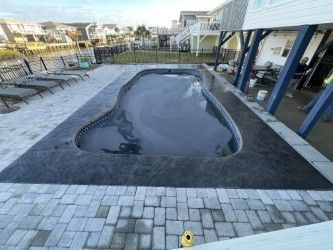 Pool with dark cover surrounded by stone patio and brick pavers, near houses.