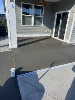 Newly poured concrete patio, adjacent to a house with a sliding glass door and windows. A drainage channel is visible.