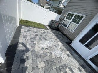 Patio with gray pavers, white fence, and house with a window and door.