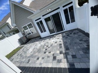 Patio with gray and black pavers, sliding glass door, and white fence.