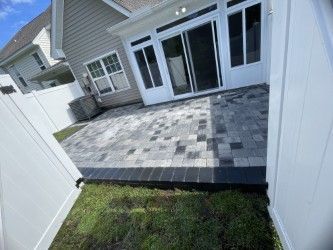 Patio with gray and black pavers, enclosed by a white fence and leading to sliding glass doors.