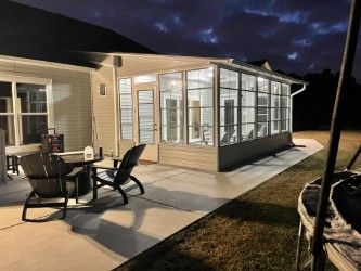 Nighttime view of a sunroom with patio furniture on a concrete slab.