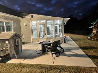 Patio with table, chairs, and playhouse under a cloudy night sky. A sunroom is visible.