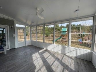 Sunroom with large windows overlooking a playground, featuring gray floors, white walls, and a ceiling fan.
