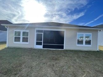 Rear exterior of a light beige house with white trim, a screened-in porch, and a grassy lawn under a cloudy sky.