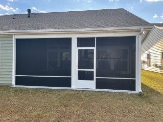 Screened-in porch attached to a house with white trim, black screens, and a white door.