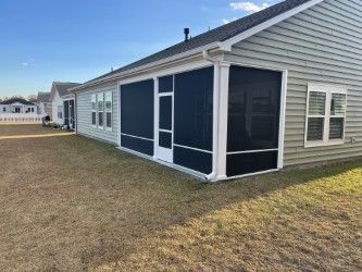 Screened-in porch attached to a light-green house; tan grass yard, blue sky.