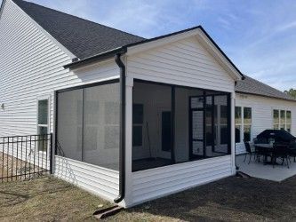 A white-sided home with a screened porch addition. Black trim, gutter, and screen frames. Sunny outdoor setting.