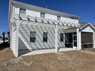 White two-story house with a pergola and screened porch, casting shadows on the side of the house under a clear blue sky.
