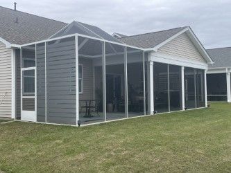 Gray screened-in porch attached to a light-colored house, with green grass in front.