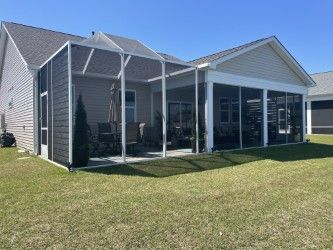 Screened-in porch attached to a light-colored house. Green grass and blue sky are visible.