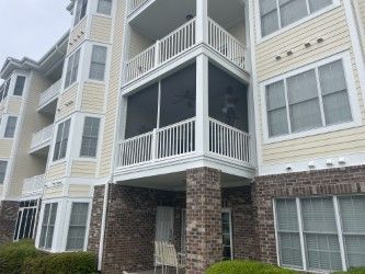 Multi-story building with white balconies and brick pillars. Dark screen-enclosed balcony. Beige exterior.
