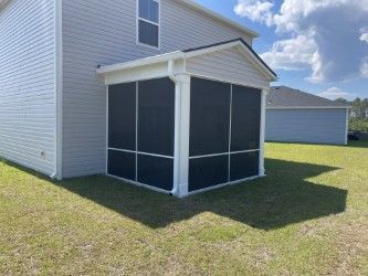 Screened porch attached to a light gray house on a grassy lawn; blue sky in the background.