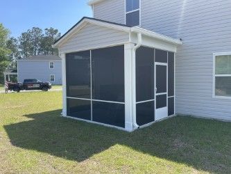 Screened porch attached to a light gray house; white trim, dark screens, and door.