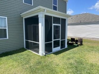 White screened porch attached to a green house with a matching white roof.