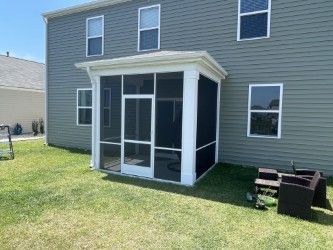 Screened porch attached to a light green house with white trim. Green lawn.