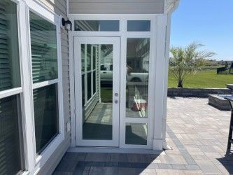 White door and windows with glass panes, leading to a sunroom. Exterior of a house with a stone patio.