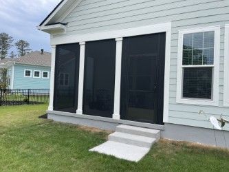 Screened-in porch with white columns, concrete steps, and a light blue house. Black screens and door. Green grass.