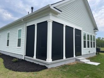 White house with black screen-enclosed porch. Landscaping includes black mulch and grass.