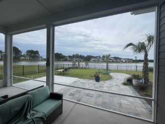 Covered patio with screens overlooking a lake, houses, and palm tree.