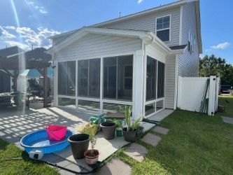 Screened porch attached to a two-story house, with patio furniture and a small wading pool in the yard.