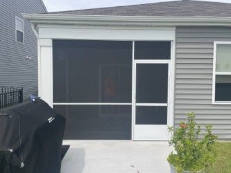 Screened-in porch with white trim, dark screens, and a door, next to a gray house with visible siding.