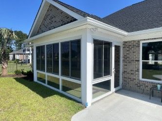 Screened-in porch attached to a brick house with a concrete patio and a grassy lawn.