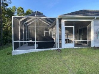 Screened-in porch attached to a house with a concrete patio, grill, and outdoor seating.