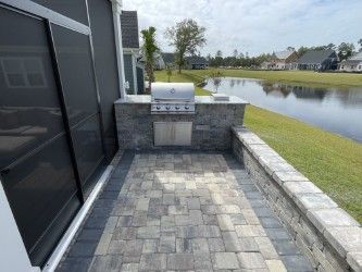Outdoor patio with built-in grill, brick pavers, and view of a lake.
