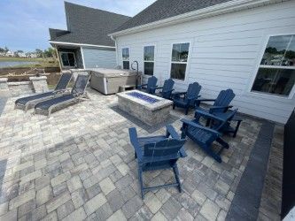Patio with blue Adirondack chairs, fire pit, hot tub, and lounge chairs next to a light blue house.