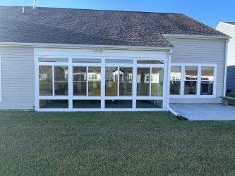 Sunroom addition with white frames, many windows, gray siding, and a concrete patio.