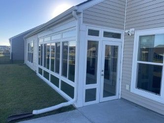 Sunroom with glass windows and door attached to a house with light tan siding.