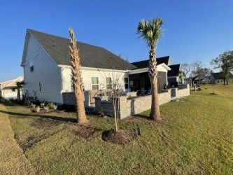 Back of a white house with a patio and palm trees on a sunny, grassy lawn.