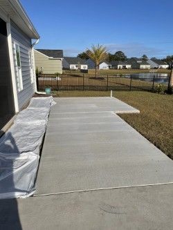 A newly poured concrete patio outside a house, with a grass yard and blue sky background.