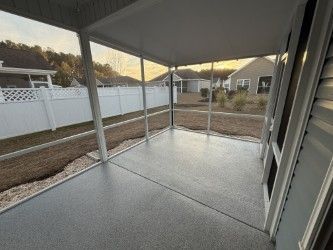Screened-in porch with gray floor, white frame, and view of backyard with white fence and houses.