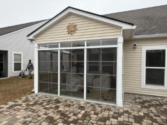 Screened-in porch attached to a beige house, with a sunburst decoration. A person is cleaning the patio.