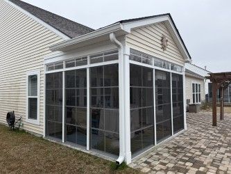A screened porch attached to a light-colored house with a brick patio and white trim.