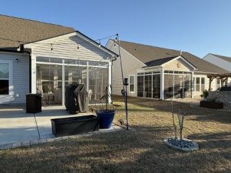 Backyard view of two houses with screened-in patios, a patio, and a grassy lawn.