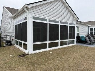 Screened-in porch attached to a white house, with a black fence and lawn in the foreground.