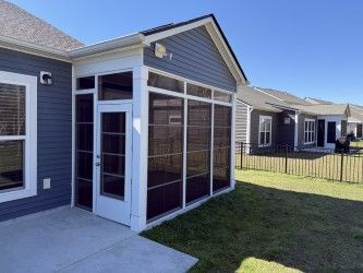 Screened porch addition on a house with blue siding, adjacent to a patio, and a grassy yard.