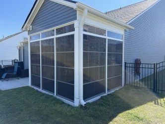 Screened-in porch attached to a house with blue siding, white trim, and a black fence.