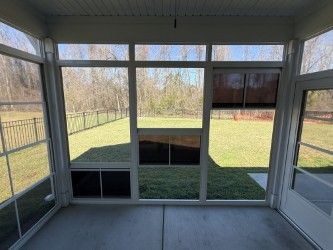 Sunroom interior overlooking a grassy backyard with a fence. Bright daylight streams in through the windows.