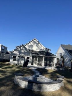 Backyard with a house, a screened porch, and a brick fire pit under a clear blue sky.