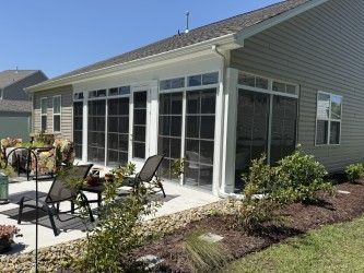Sunroom with screened windows, patio, and outdoor seating under a blue sky.