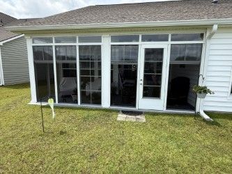 Sunroom with white frames and doors attached to a white house, on a green lawn.