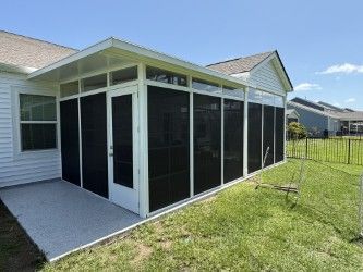 Screened-in porch attached to a white house with a concrete patio, green grass, and blue sky.