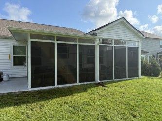 Screened porch attached to a white house with a grassy lawn, under a partly cloudy sky.
