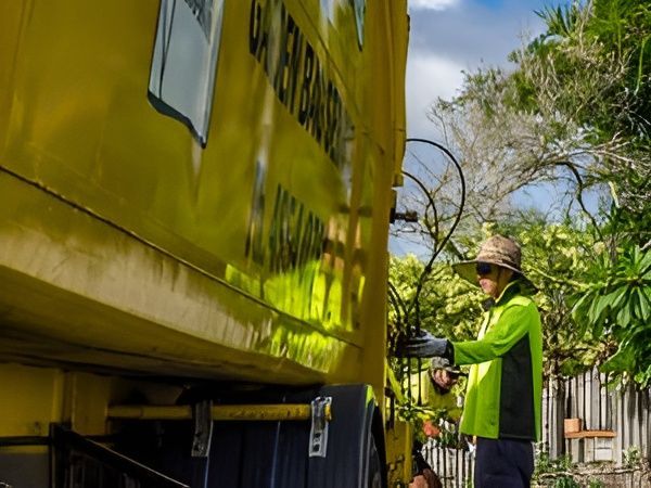 Green Garbage Truck Lifts a Blue Trash Bin to Empty It — Bobs Bags & Bins in Mackay, QLD