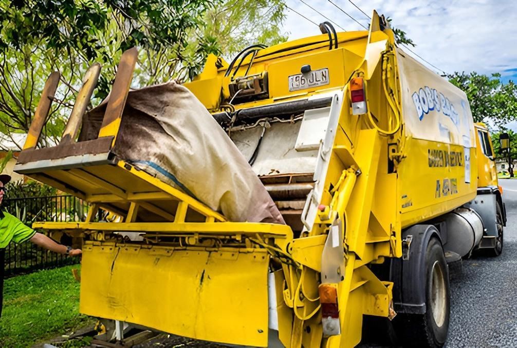 Yellow Garbage Truck Lifting a Large Bag of Trash — Bobs Bags & Bins in Mackay, QLD