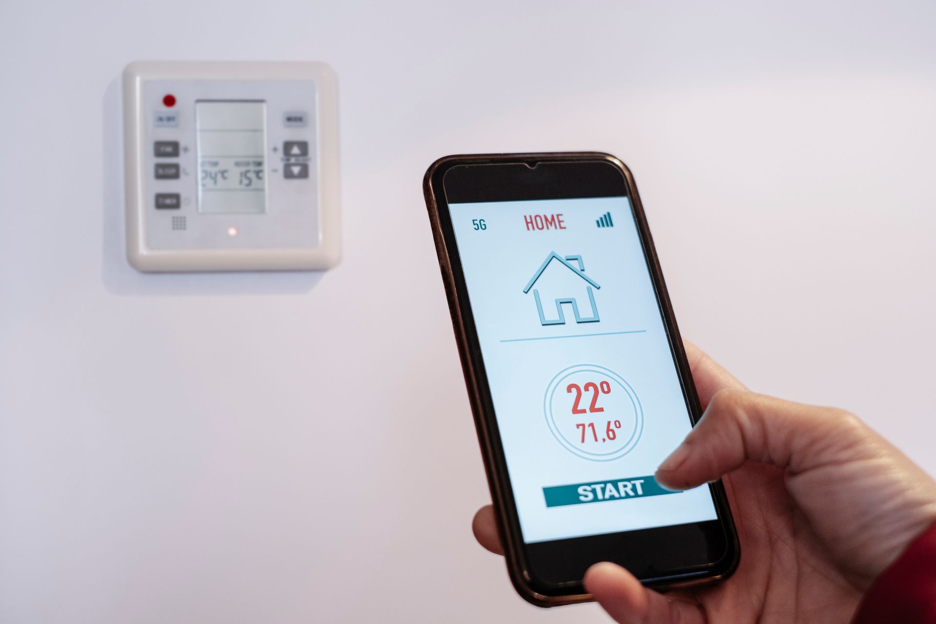 Person uses phone app to control a white wall thermostat, displaying 22°C/71.6°F.